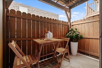 A wooden table with two chairs and a vase of flowers on a patio.